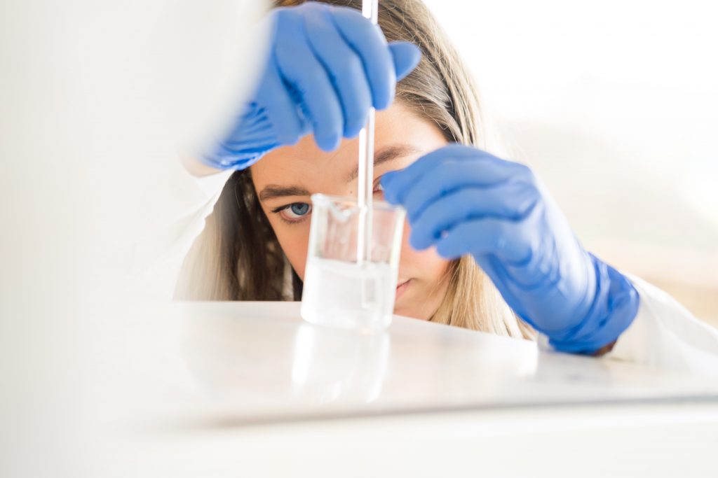 Ung pige laver kemiforsøg på gymnasium med blå handsker og reagensglas